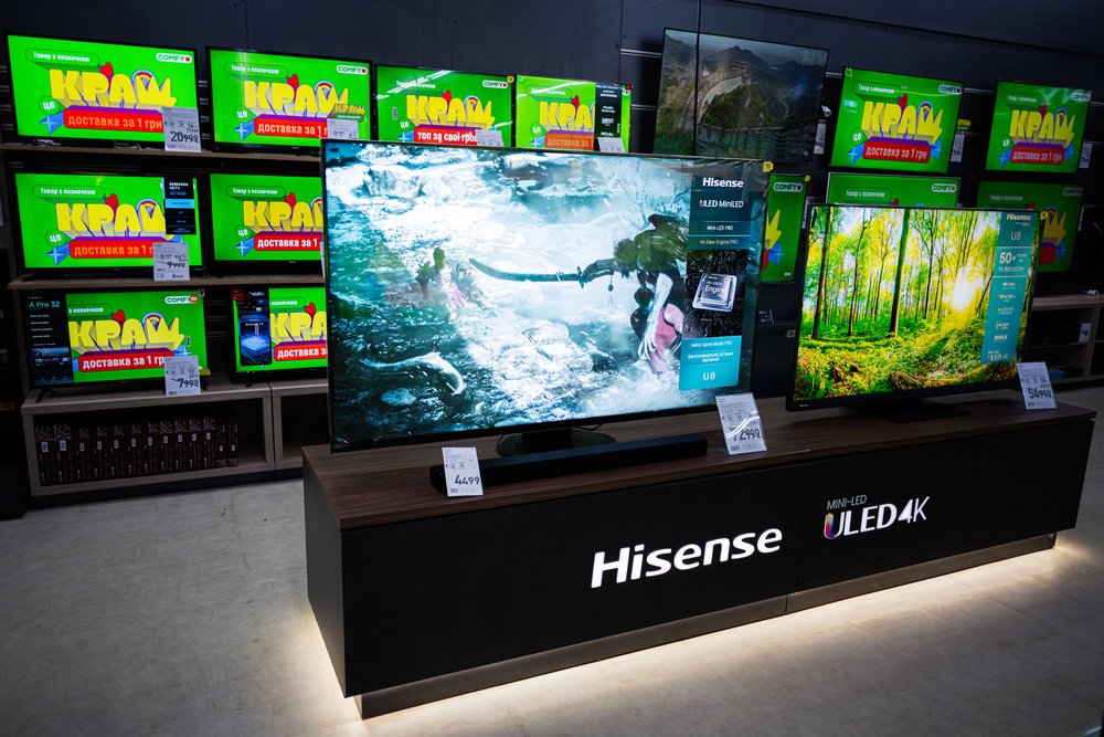 Izložba Hisense 4K ULED televizora, uključujući neke od najboljih modela, u trgovini elektronike, sa šarenim natpisima za rasprodaju na televizorima u pozadini.