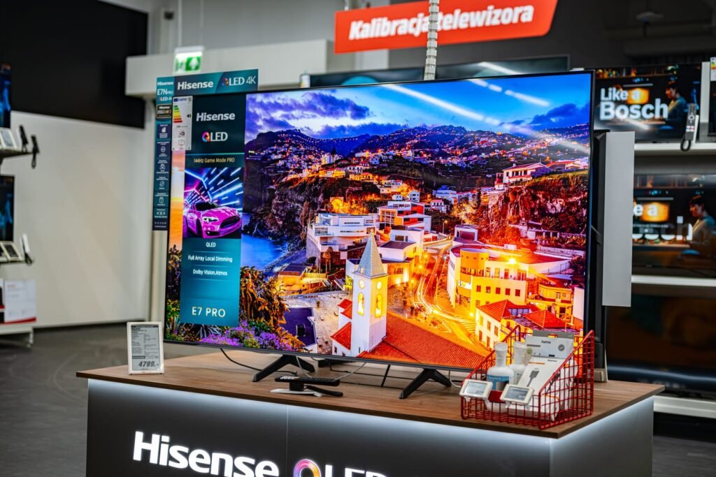 Hisense TV LED 4K Smart TV izložen je na štandu u trgovini elektronike, prikazujući živopisnu sliku gradskog pejzaža. Specifikacije televizora i cijene vidljive su u blizini, što upućuje na najnoviji model iz 2025. i pozitivna iskustva kupaca.