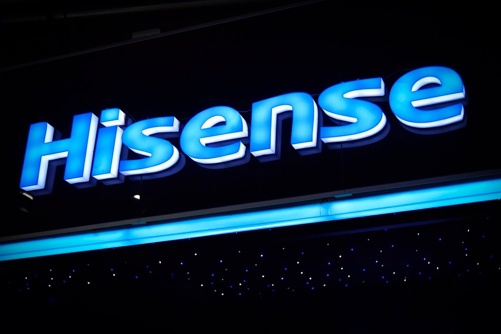 Osvijetljeni Hisense logotip u plavoj i bijeloj boji na tamnoj pozadini s malim plavim svjetlima ispod, evocira pozitivna Hisense TV iskustva i podsjećajući na najbolji model ovog brenda.