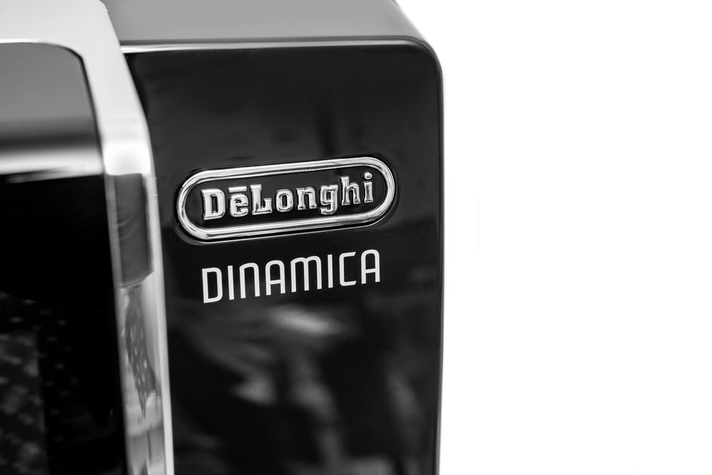 Krupni plan DeLonghi Dinamica aparata za espresso, reklamiranog kao najbolji aparat za kavu 2025, s nazivom marke i modela na elegantnoj crnoj vanjštini.