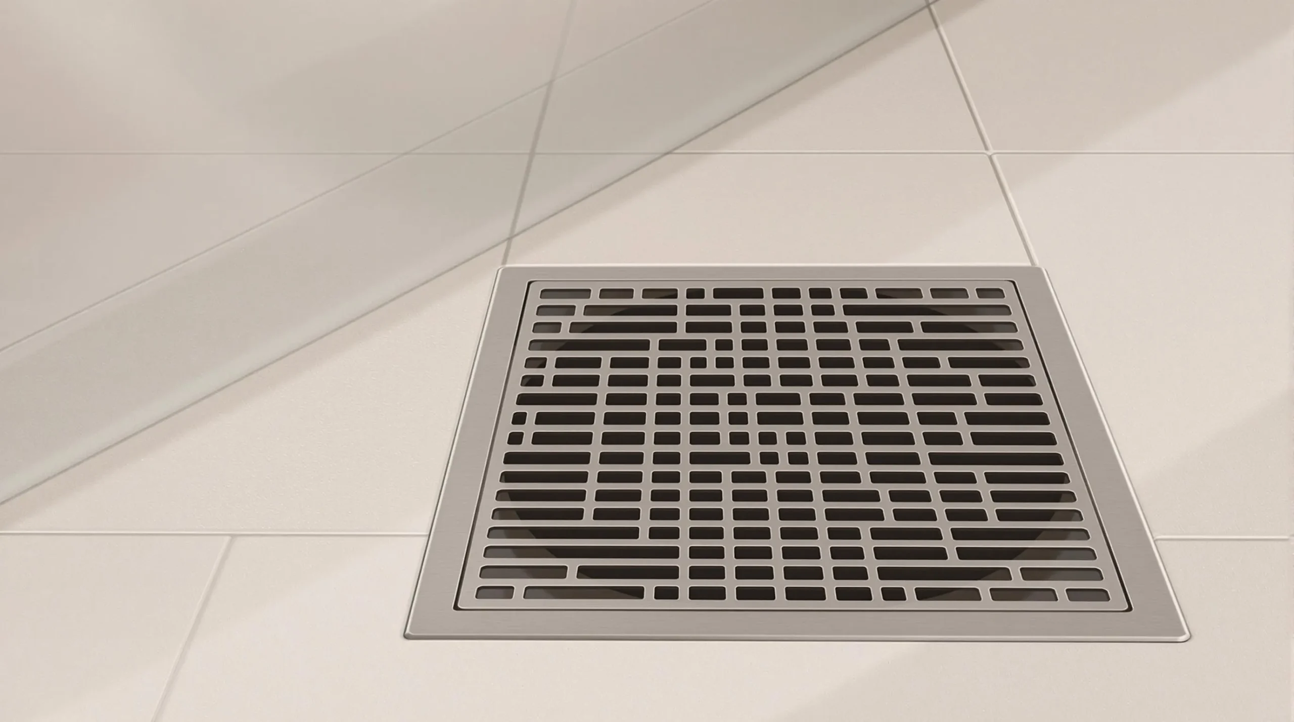 Kvadratni metalni podni sifon s geometrijskim mrežastim dizajnom ugrađen je u svijetle pločice na podu, dodajući moderan dodir svakoj kupaonici.