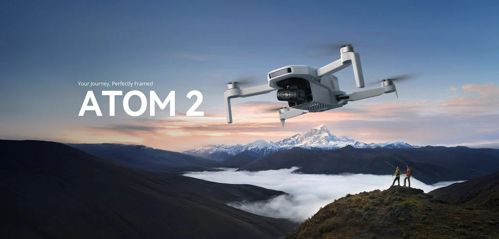 Dron leti iznad planinskog krajolika u zalazak sunca, s dvije osobe koje stoje na vrhu brda i tekstom ATOM 2 prikazanim s lijeve strane - idealna inspiracija ako se pitate koji dron kupiti.