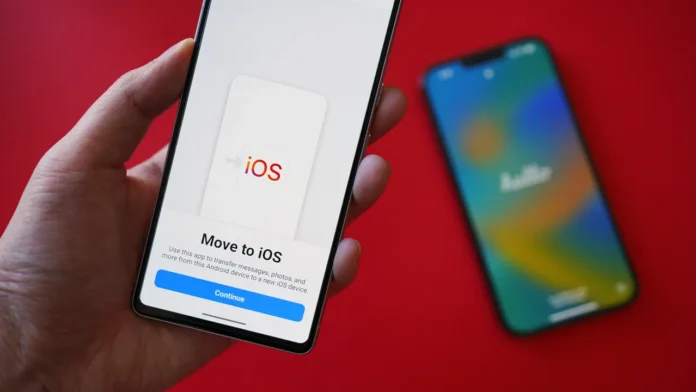 Ruka drži pametni telefon na kojem se prikazuje aplikacija Move to iOS, jedna od najboljih aplikacija za prijenos podataka na novi mobitel, s mutnim iPhoneom i crvenom pozadinom u sceni.