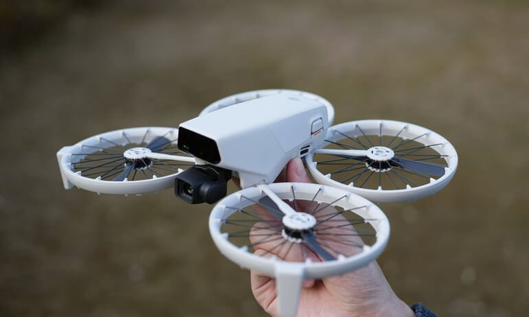 Ruka drži mali bijeli kvadkopter dron sa štitnicima propelera na otvorenom - idealan za one koji traže preporuke dronova ili se pitaju "koji dron kupiti" za početnike.