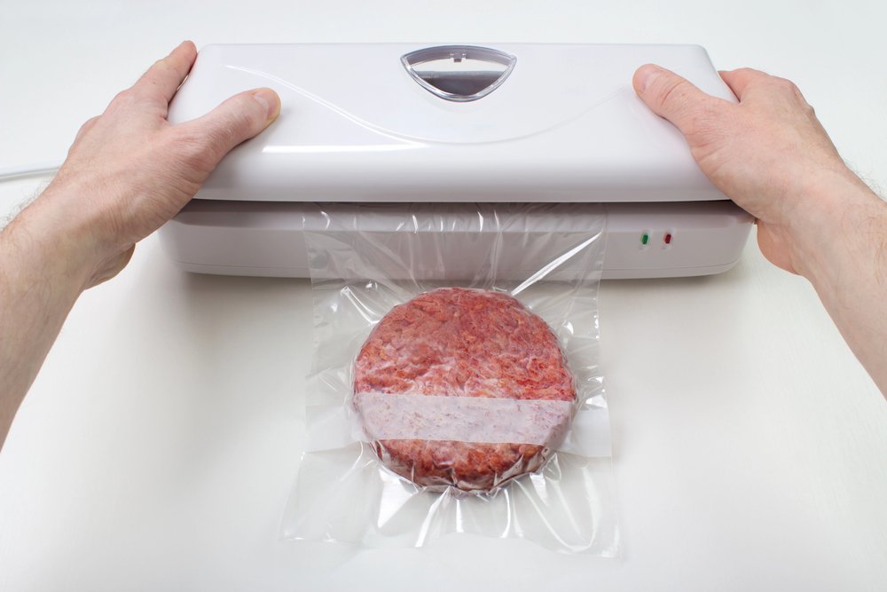 Osoba koristi aparat za vakumiranje kako bi vakuumski zatvorila sirovi hamburger u plastičnu vrećicu na bijeloj površini - savršeno za one koji traže Najbolji odabir u 2025. godini.