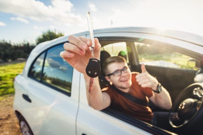 Nasmijana osoba sjedi u automobilu i jednom rukom drži ključ od auta kroz prozor, a drugom pokazuje palac gore, sretna zbog svog brzog izračuna PPMV-a pomoću PPMV kalkulatora.