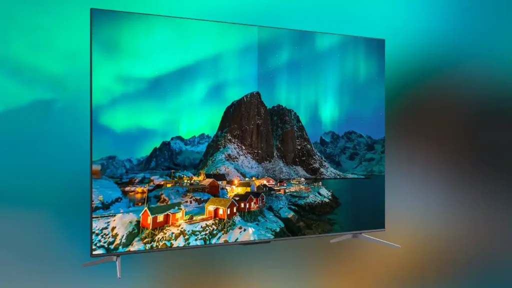 Veliki televizor ravnog ekrana prikazuje živopisni planinski krajolik sa sjevernim svjetlima i malim kućama, nasuprot zamućenoj pozadini - impresivan prizor savršen za vašu sljedeću kupnju TCL televizora.