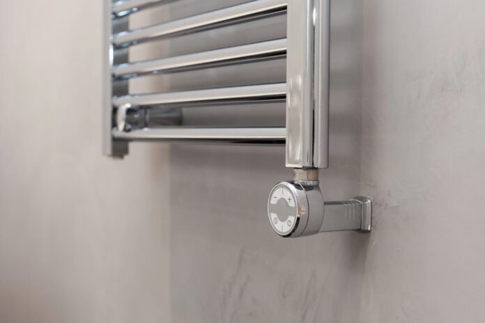 Izbliza moderna, kromirana grijalica za kupaonicu s okruglim ventilom za regulaciju temperature postavljena na zid svijetle boje—preporuka za najbolju grijalicu za elegantan stil i učinkovito grijanje.