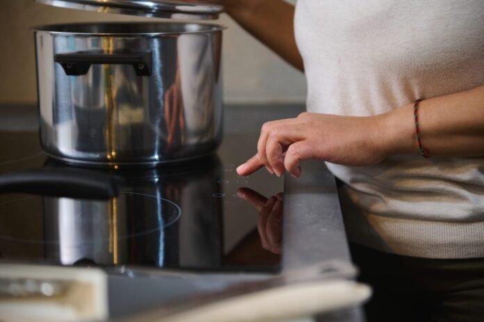 Osoba koristi dodirnu ploču na indukcijskoj ploči dok drži poklopac lonca od nehrđajućeg čelika.