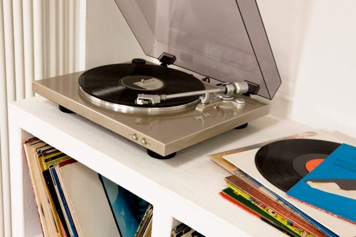 Gramofon na bijeloj polici, svira ploča, s još ploča pohranjenih ispod i hrpom pokraj nje—savršena scena za ljubitelje glazbe i ona koja traži najbolju gramofoni preporuka.
