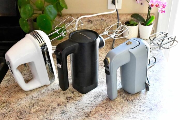 Tri pekari ručni mikseri u bijeloj, crnoj i sivoj boji stoje uspravno na kuhinjskoj radnoj površini u blizini biljaka u lončanicama i električne utičnice, spremni da vam pomognu u stvaranju najboljih recepata s najboljim mikserima.